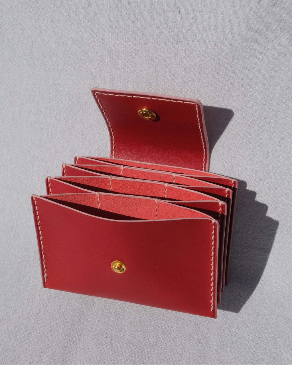 A red leather card holder wallet with multiple card slots, shown open on a light gray textured background.